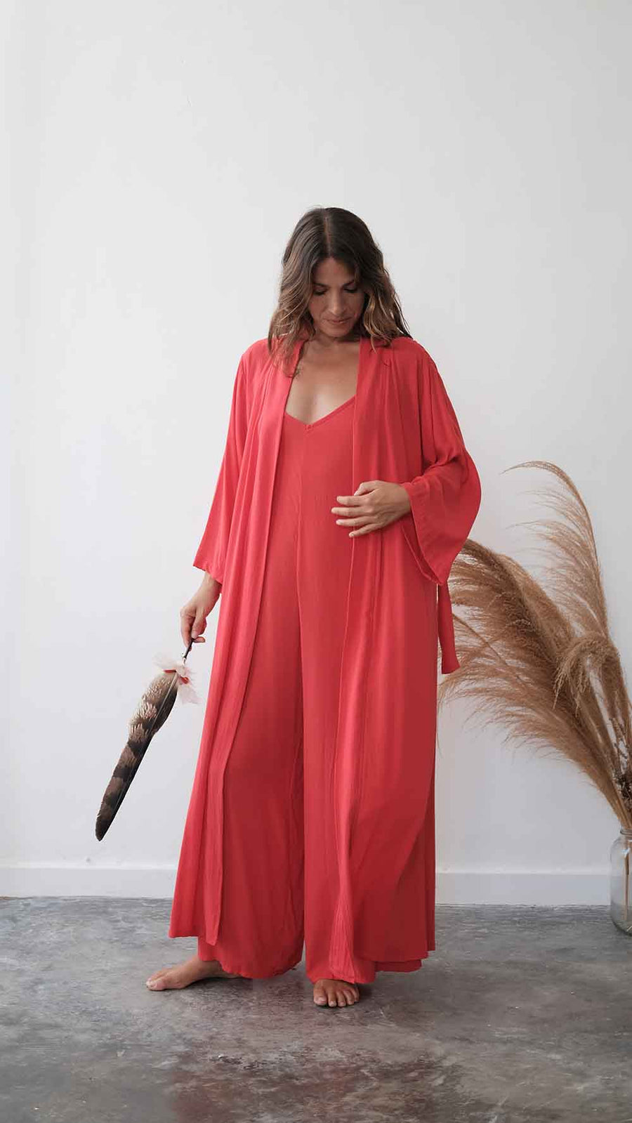 Woman in a coral dress holding a feather duster against a white wall.