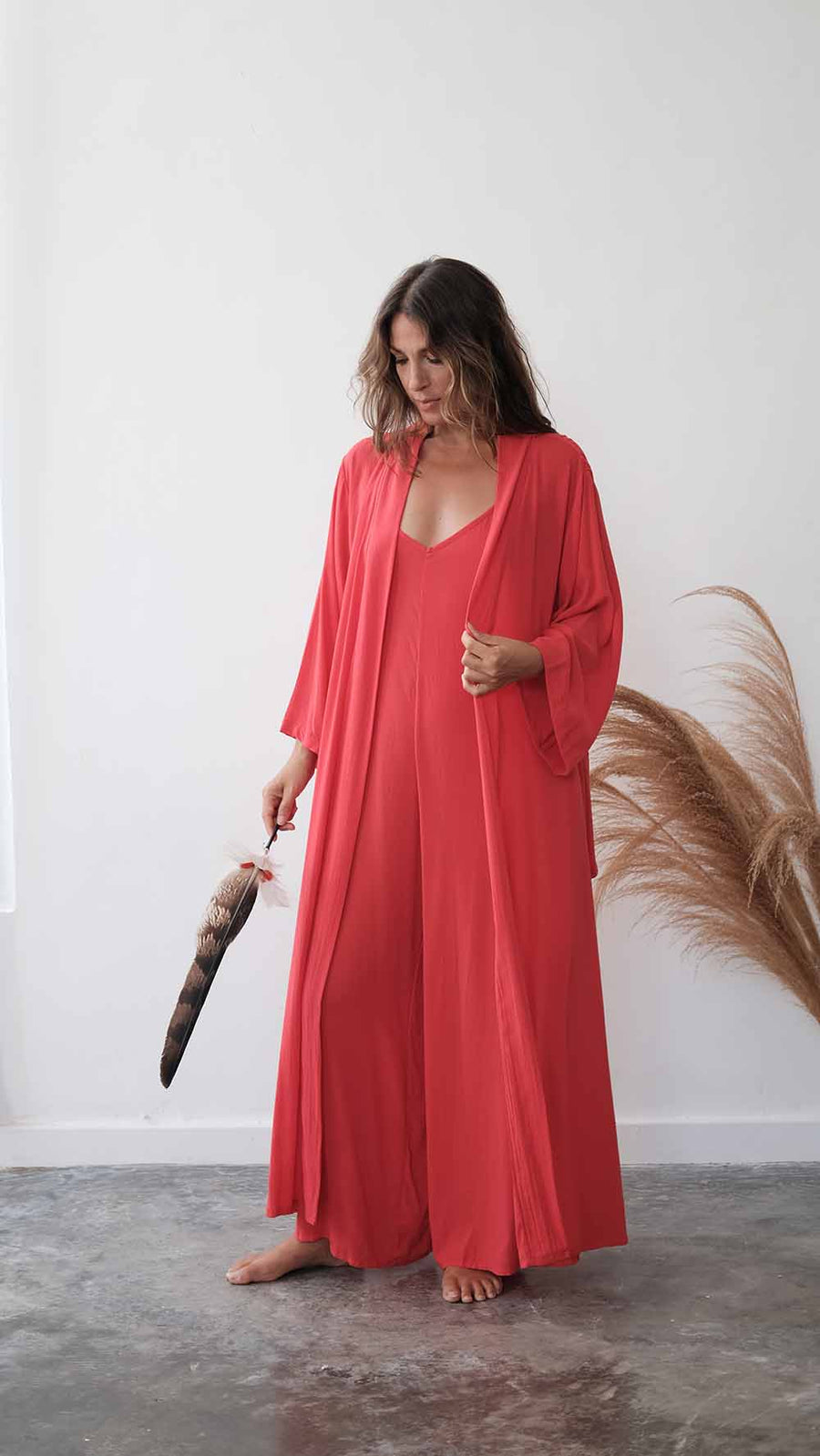 Woman in a red dress holding a feather duster against a white wall.