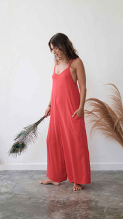 Woman in a coral jumpsuit holding a plant against a white wall.