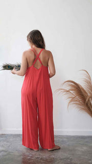 Woman wearing a red jumpsuit holding a bouquet of flowers against a white wall.