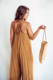 Woman in a mustard yellow dress holding a woven bag against a white background