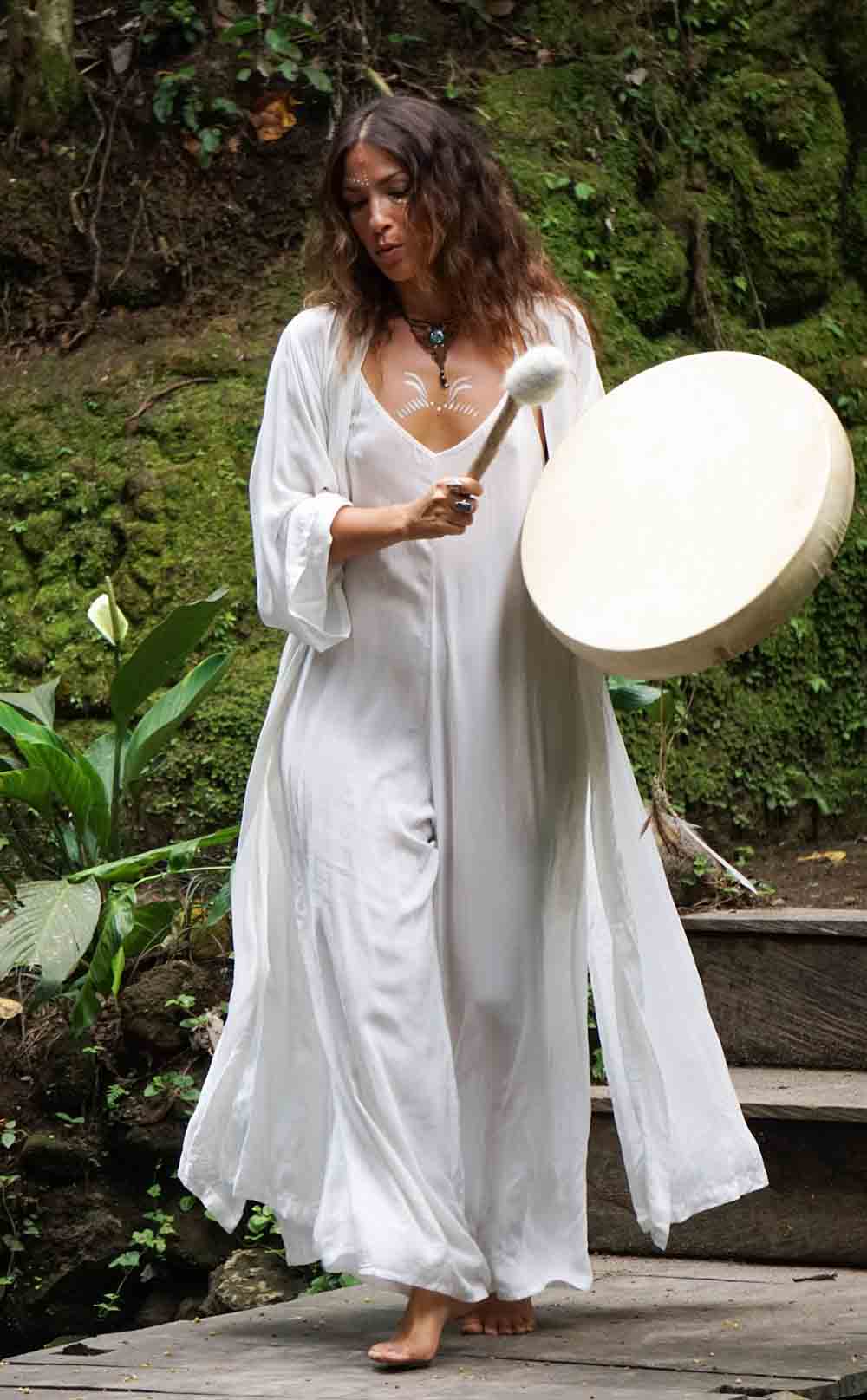 Woman in a white dress holding a large drum outdoors