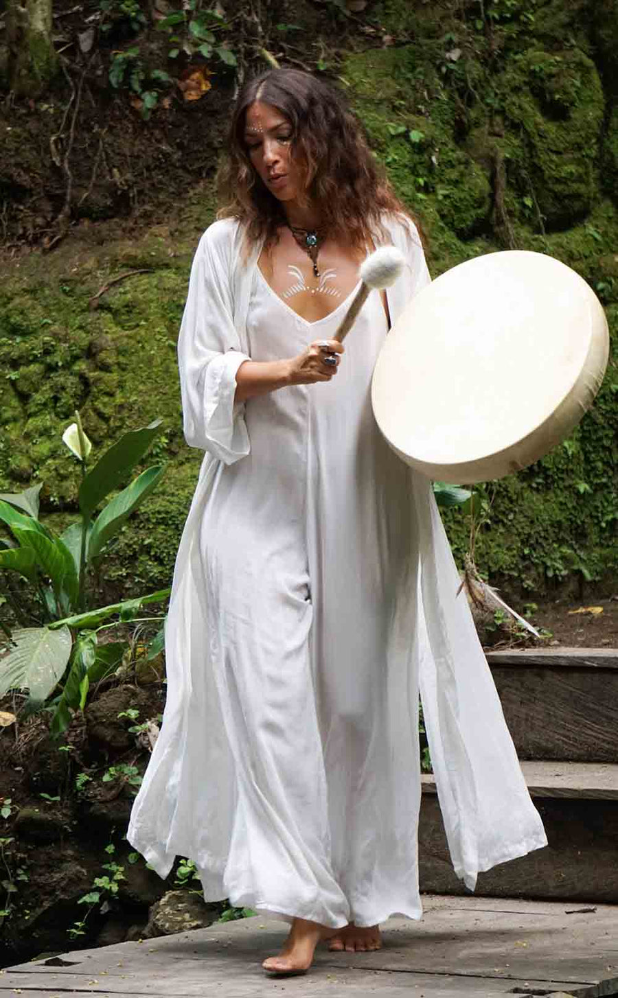 Woman in a white dress holding a large drum outdoors