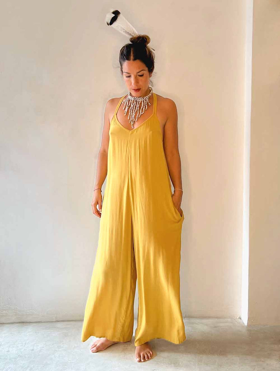 Woman wearing a yellow jumpsuit against a white wall.