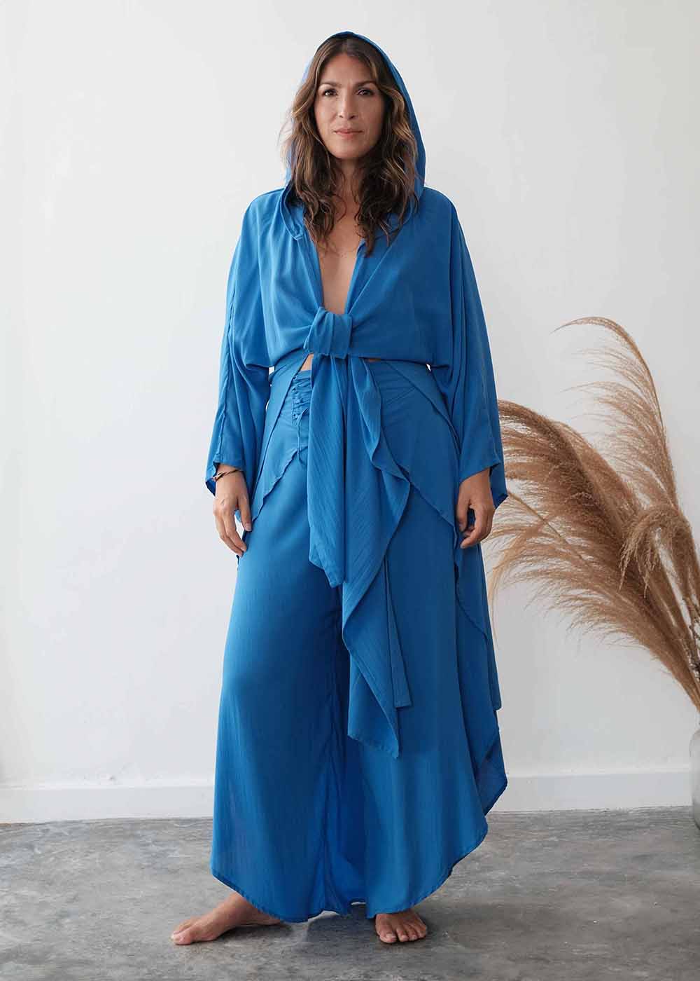 Woman wearing a blue dress with a hood against a white wall.