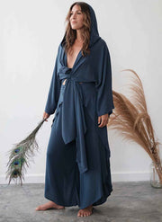 Woman wearing a long, dark blue robe holding peacock feathers against a white wall.