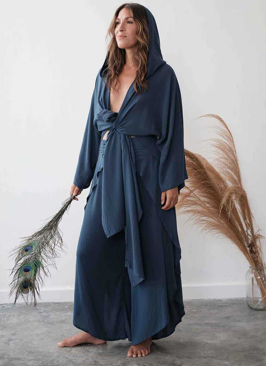 Woman wearing a long, dark blue robe holding peacock feathers against a white wall.