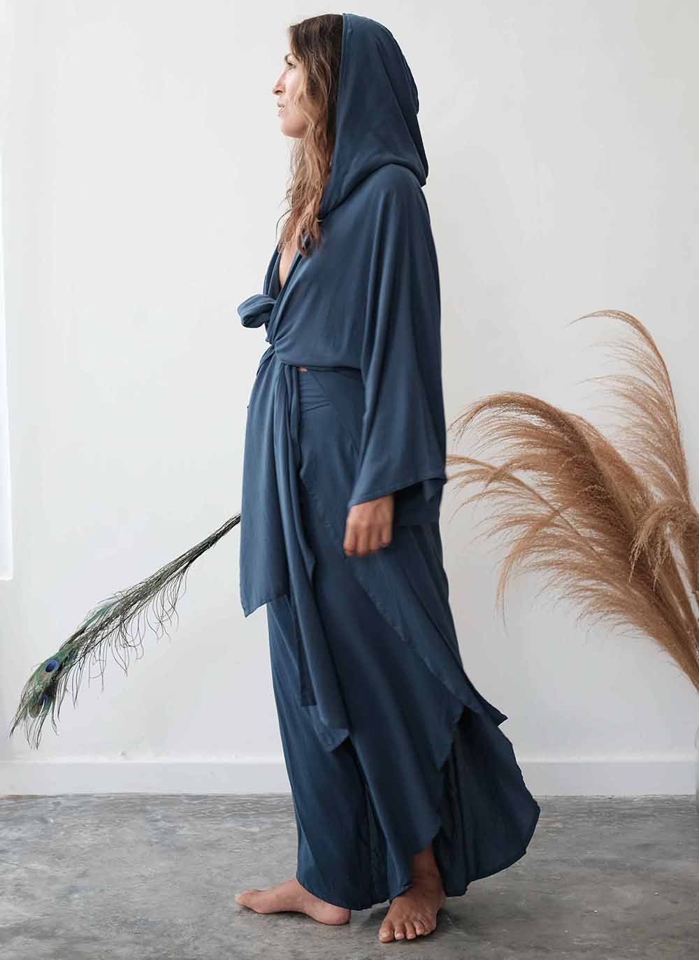 Woman wearing a long, dark blue robe standing against a white wall with decorative elements.