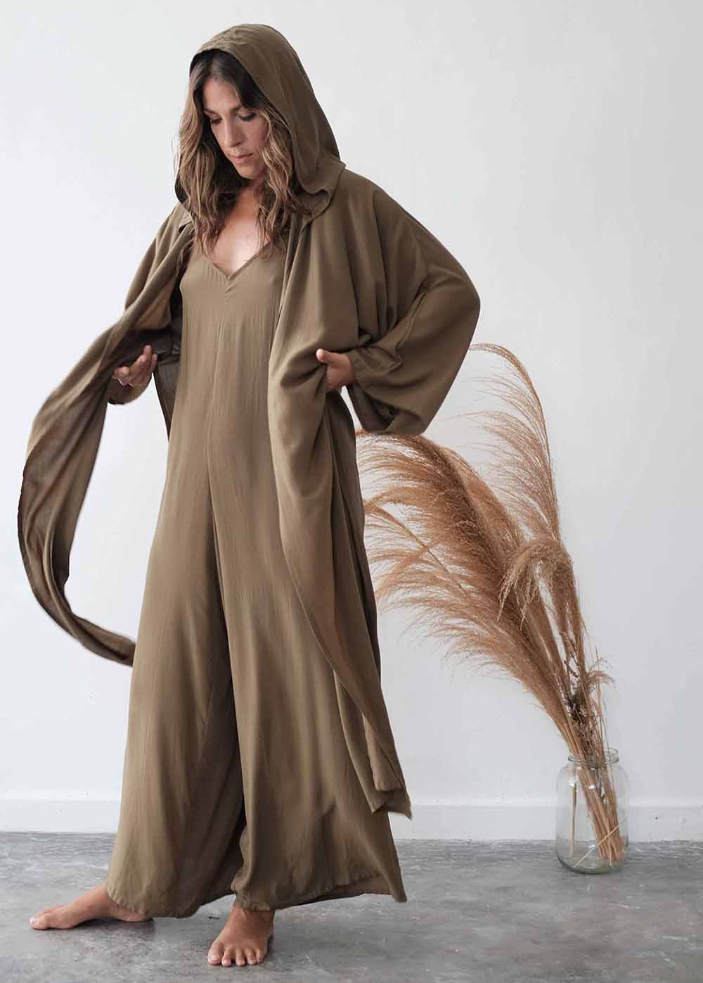 Woman wearing a long brown robe with a hood in a minimalistic setting.