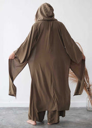 Person wearing a brown hooded garment against a white wall.
