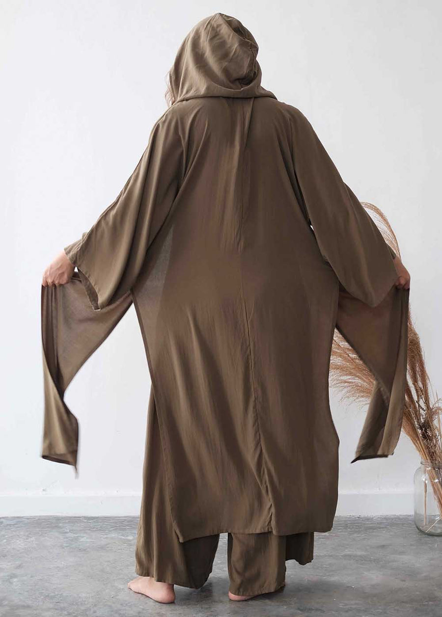 Person wearing a brown hooded garment against a white wall.