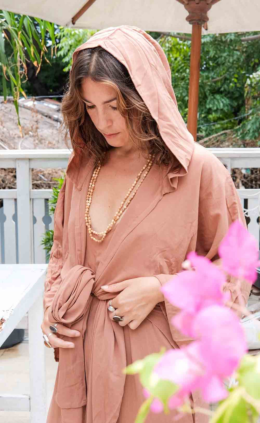 Woman wearing a pink hijab and dress outdoors with greenery in the background