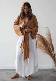 Woman wearing a brown robe over a white dress with pampas grass in the background