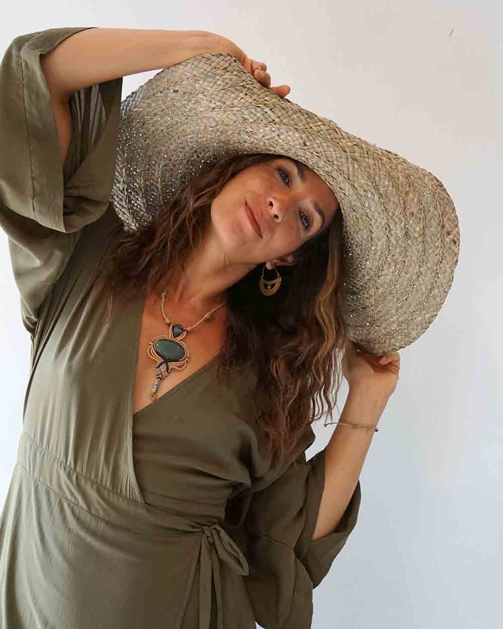 Woman wearing a large straw hat and green dress against a white background