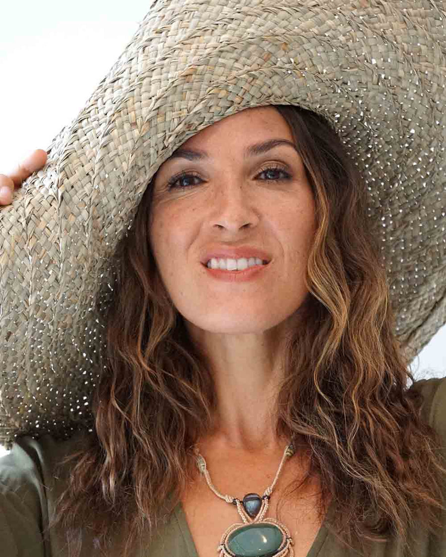 Woman wearing a straw hat and green top with a necklace, outdoors.