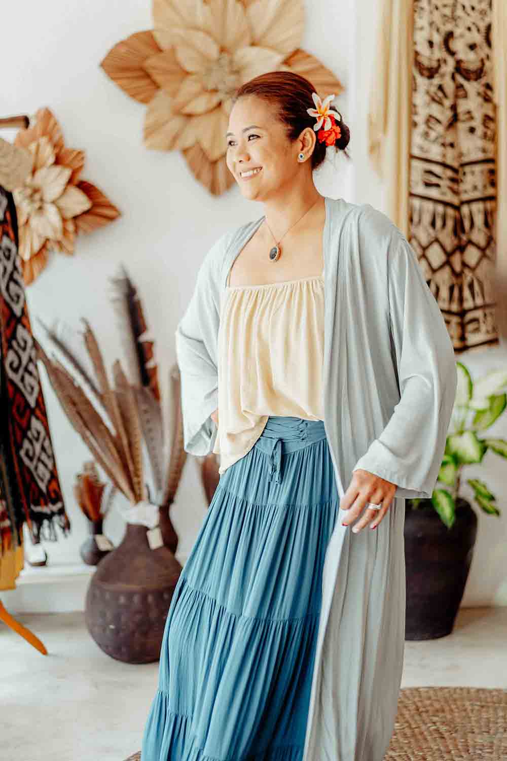 Woman wearing a light gray cardigan over a beige top and blue skirt in a decorative room.
