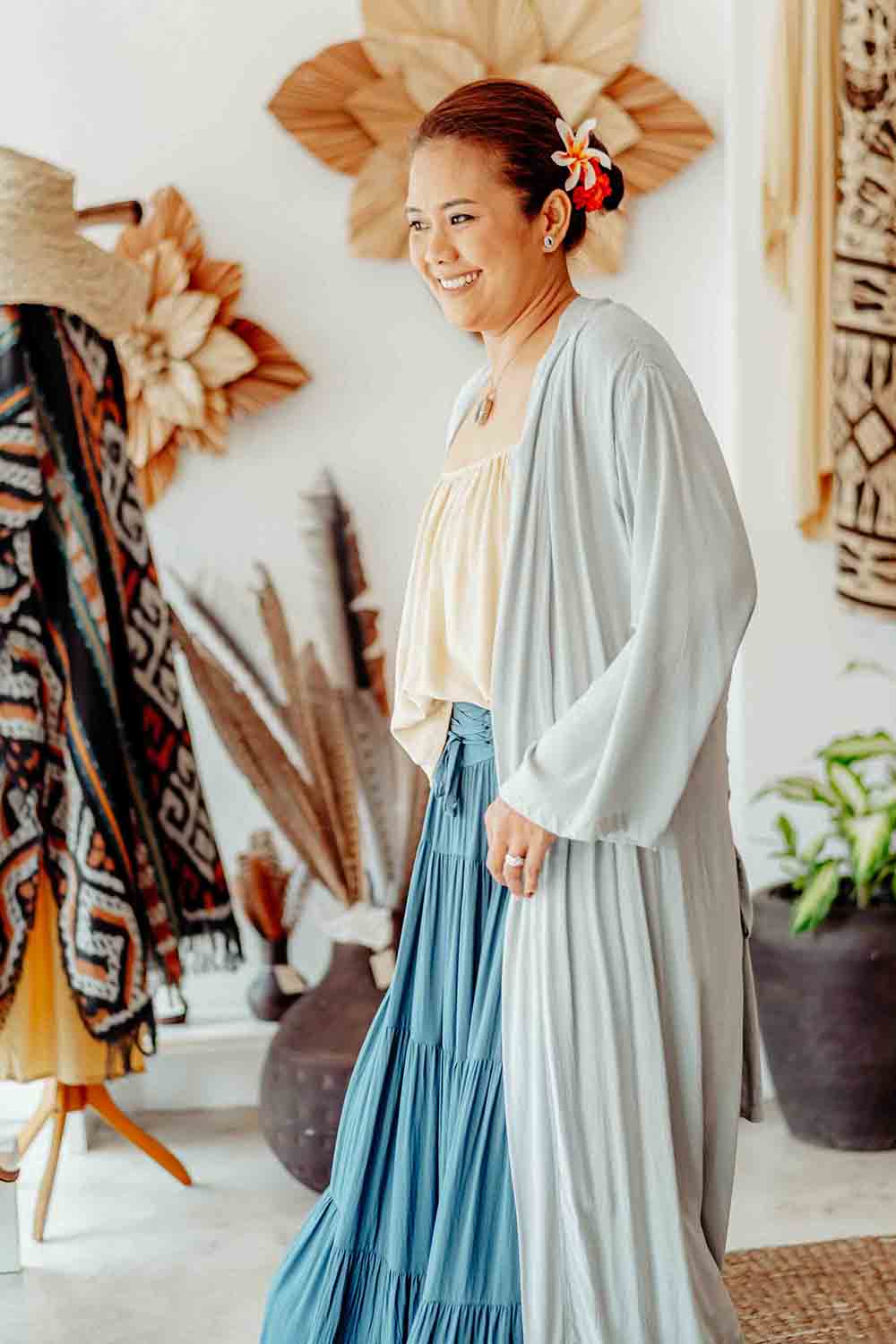 Woman in a light blue cardigan and blue skirt standing in a room with decorative items.