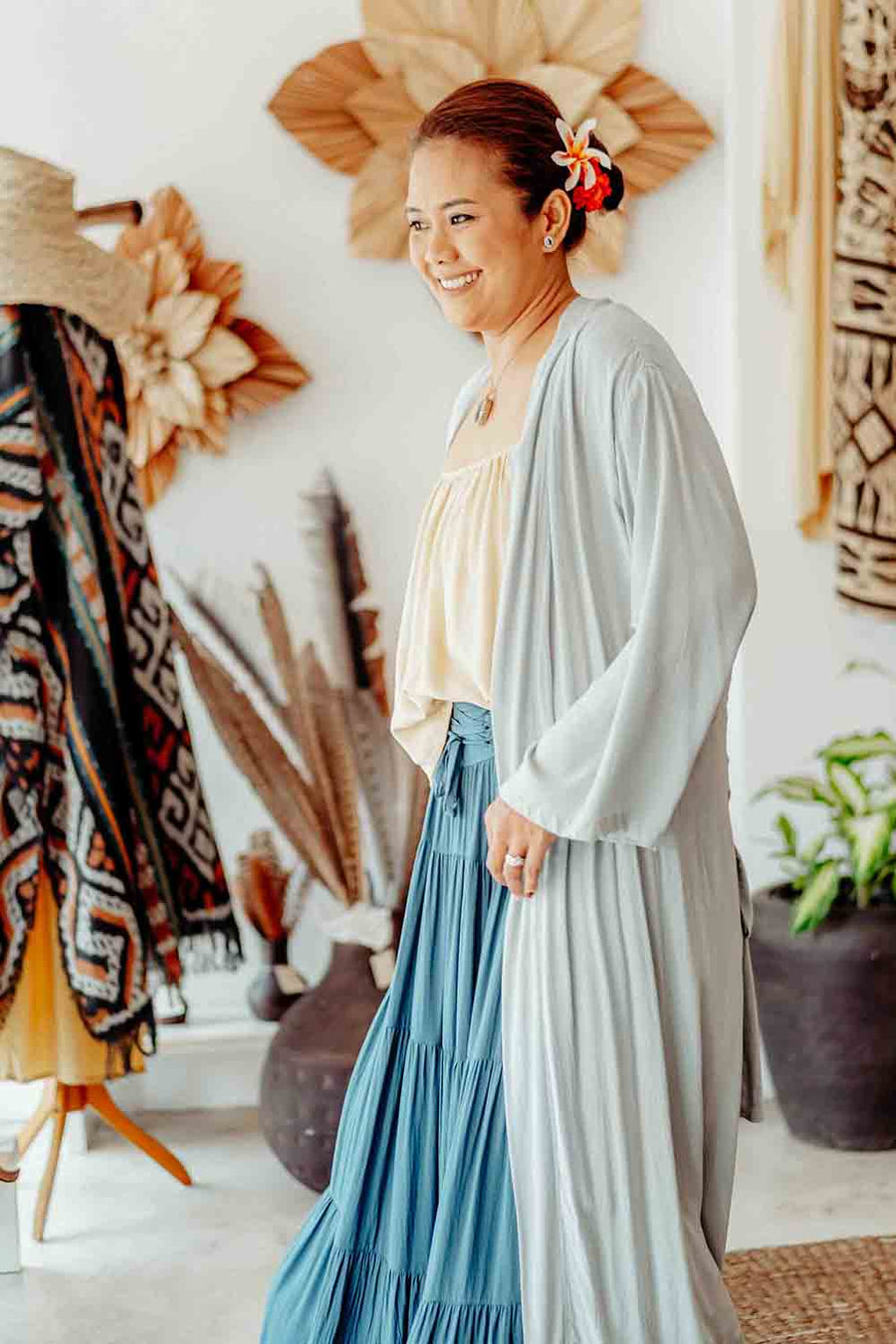 Woman in a light blue cardigan and blue skirt standing in a room with decorative items.