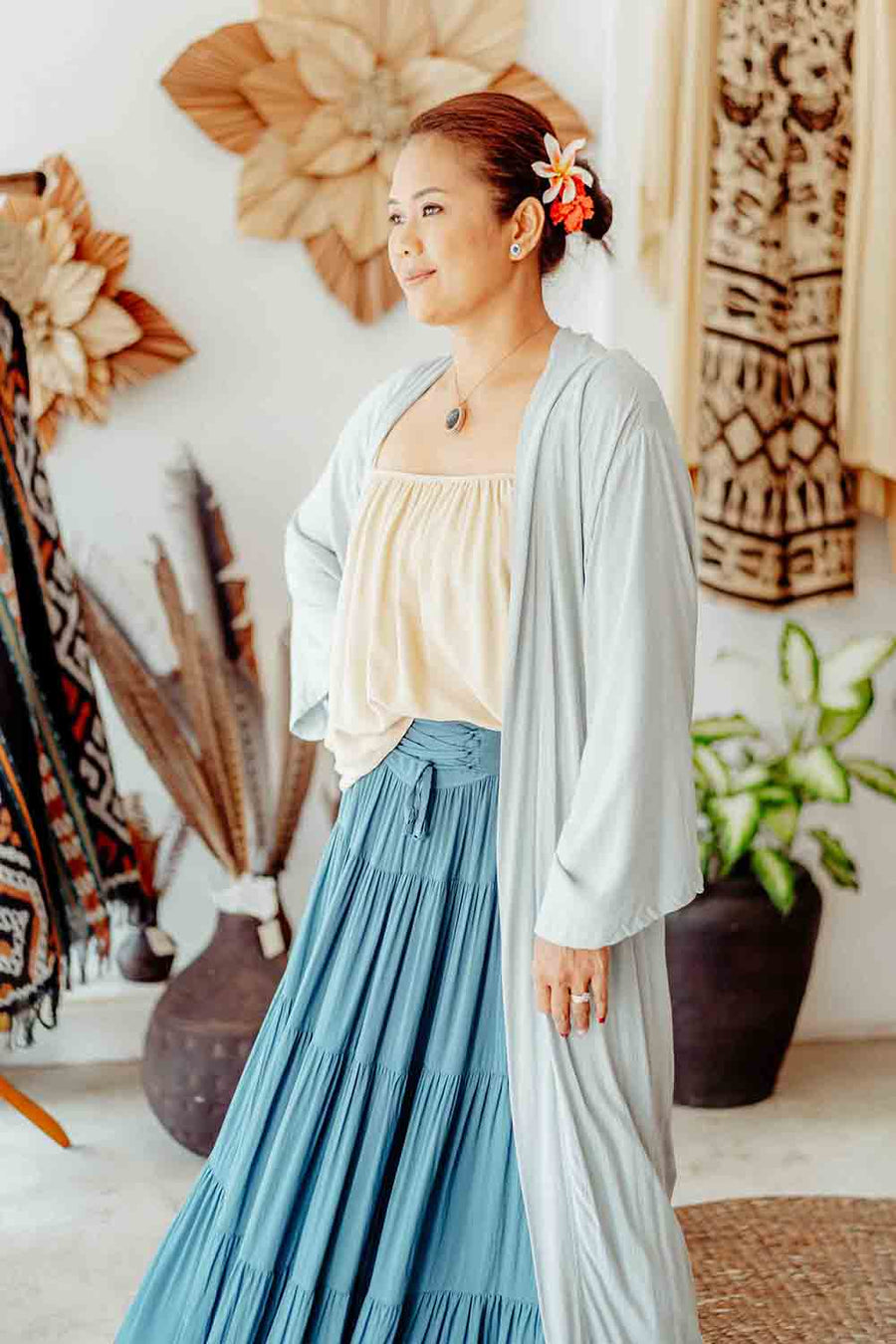 Woman in a light blue cardigan and blue skirt standing in a room with decorative elements.
