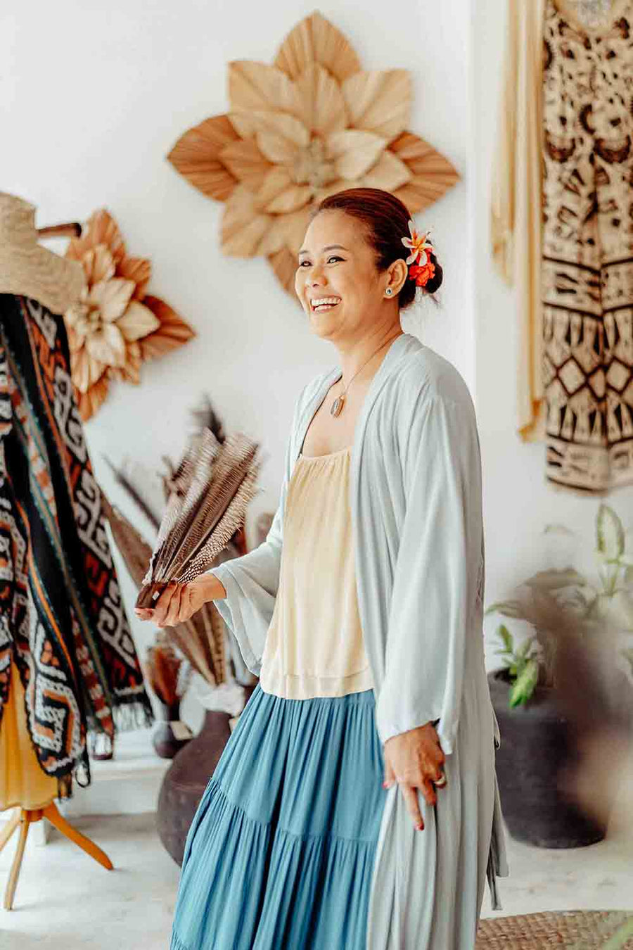 Woman in a blue dress and gray cardigan standing in a room with decorative wall art and plants.
