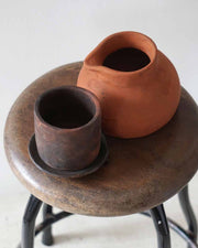 Two terracotta pots on a round wooden stool with a white background