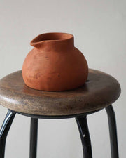 Terracotta pot on a wooden stool against a plain background