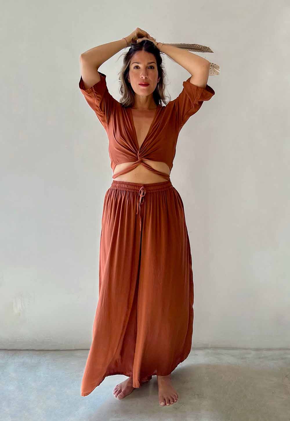 Woman wearing a rust-colored outfit with a top and long skirt against a plain background