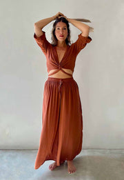Woman wearing a rust-colored outfit with a top and long skirt against a plain background