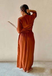 Woman in a rust-colored dress standing against a plain background