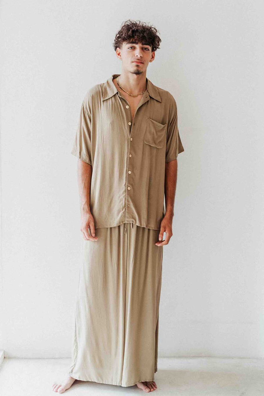 Man wearing a beige shirt and pants against a white background