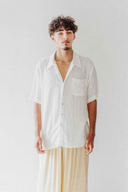 Man wearing a white shirt and beige pants against a plain background