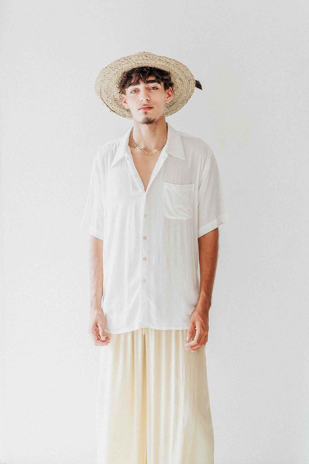 Person wearing a white shirt and straw hat against a plain background