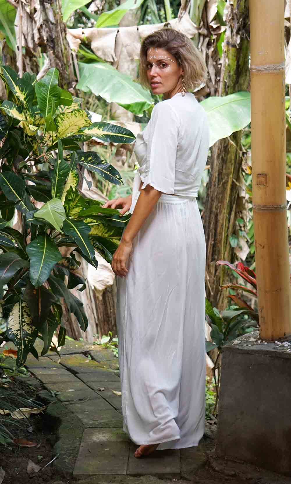 Woman in a white dress standing in a lush, tropical garden.