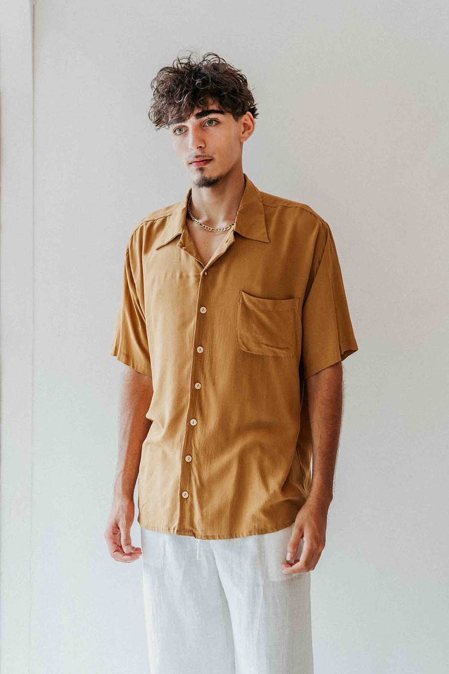 Man wearing a mustard yellow shirt with a plain background