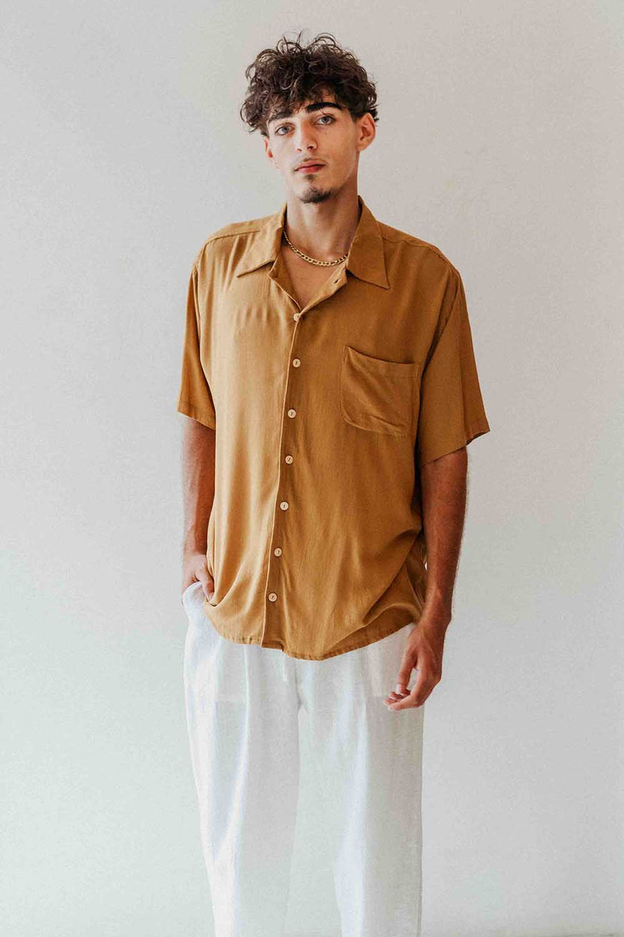 Man wearing a mustard yellow shirt and white pants against a plain background