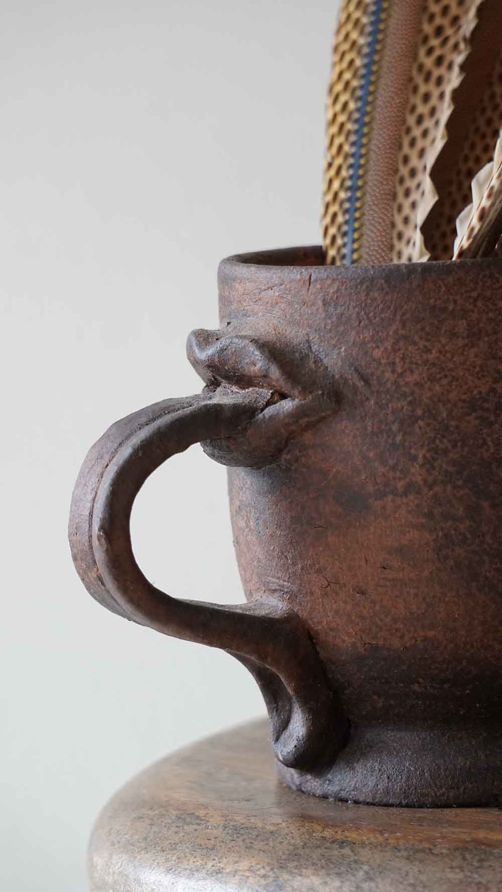 Close-up of a rustic brown ceramic mug with a handle on a light gray background