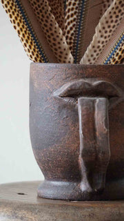 Close-up of a rustic brown ceramic mug with a handle, featuring a patterned fabric background.