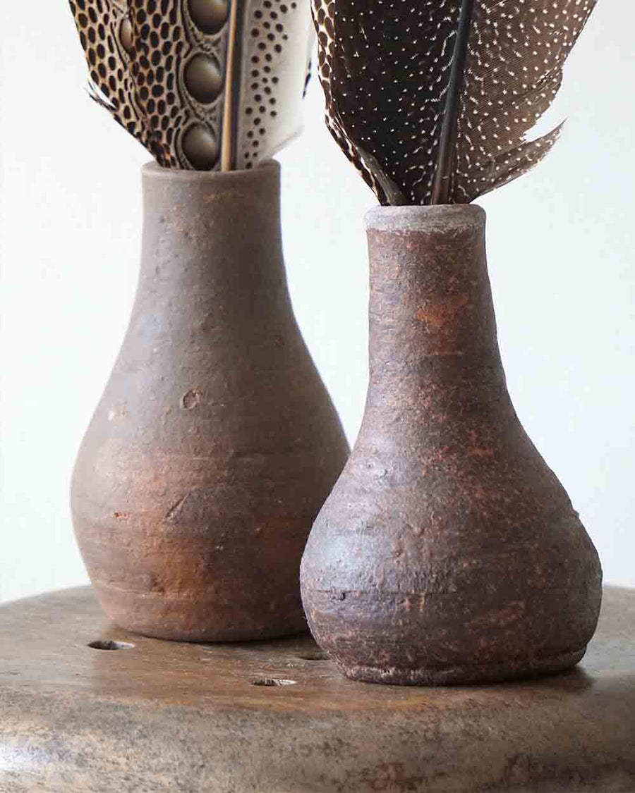 Two rustic brown ceramic vases with feathers on a wooden surface.