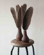 Decorative vase with feather-like design on a wooden stool against a plain background
