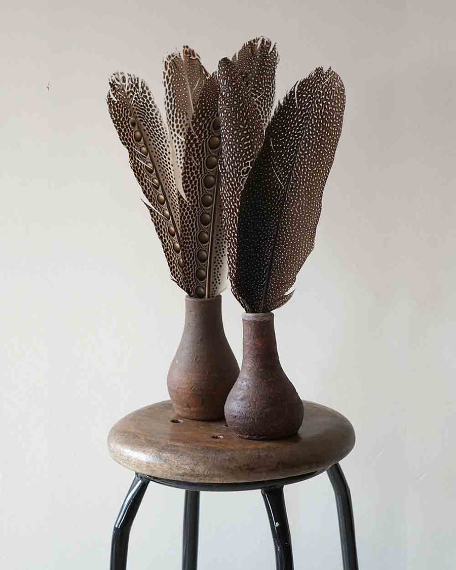 Decorative vase with feather-like design on a wooden stool against a plain background