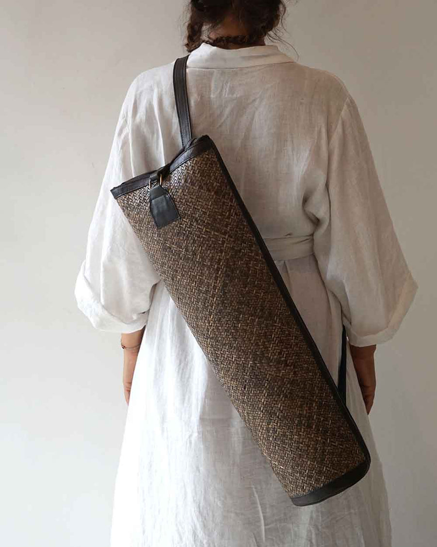 Person holding a woven yoga mat bag over their shoulder against a plain background